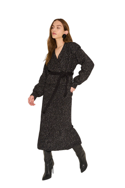 Woman wearing a black textured dress with long sleeves and a belt on a white background