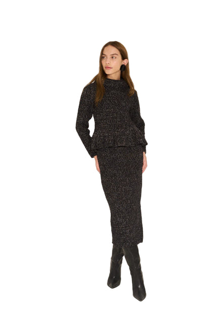 Woman wearing a black textured outfit with a top and skirt on a beige background