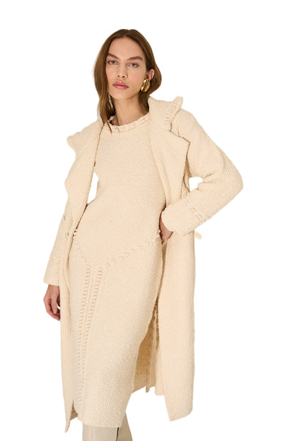 Woman wearing a long beige coat against a plain background