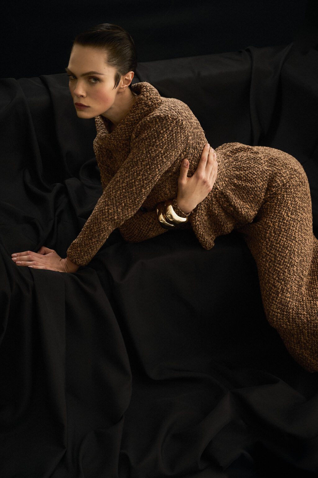 Person wearing a brown knitted outfit sitting on a black background