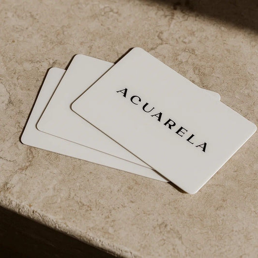 Three white cards with 'ACUARELA' printed on them, lying on a textured surface.